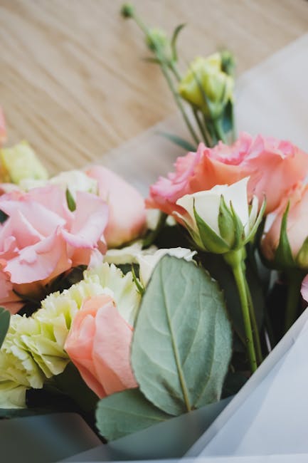 Close-up view of a fresh floral bouquet featuring pale pink and cream Lisianthus flowers with delicate, ruffled petals. The arrangement includes vibrant green leaves and stems, with some buds yet to f