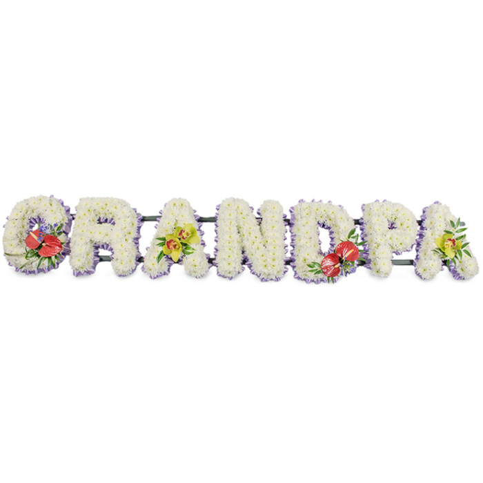 A beautifully crafted funeral flower arrangement spells the word "GRANDPA" in bold capitals, stretching horizontally across the frame against a bright, uncluttered white background so the design can be appreciated in full. Each individual letter is generously covered in pristine white chrysanthemums, the small, tightly ruffled petals packed so closely that the surface appears almost like a soft, snowy blanket. This dense texture gives the tribute a sense of tenderness and tranquillity, ideal for a final farewell. At the base of every letter, a band of pale lavender ribbon provides a neat, discreet border. This hint of lilac gently outlines the word, lending refinement and slight colour contrast without overpowering the simplicity of the white blooms. Supporting bars, finished in a deep green, run beneath the letters to keep the tribute stable and aligned, ready to be placed on a hearse or by a graveside in Palmers Green Cemetery or a nearby chapel. Carefully positioned accent sprays break the white expanse with meaningful colour. The opening "G" is decorated with a cluster of rich red anthuriums, their heart-shaped, glossy petals and central yellow spadices nestled among dark green leaves, evoking devotion and respect. The first "A" features a graceful group of yellow-green orchids, their sculpted petals and buds creating a refined, contemporary look framed by fresh foliage. Mirroring the "G", the central "D" bears another spray of vibrant red anthuriums and greenery, drawing the gaze towards the centre. On the final "A", a matching arrangement of yellow-green orchids balances the composition. This personalised "GRANDPA" tribute looks like the kind of bespoke piece a local Palmers Green family might order to honour a beloved grandfather, combining quiet elegance with a clear, heartfelt message.