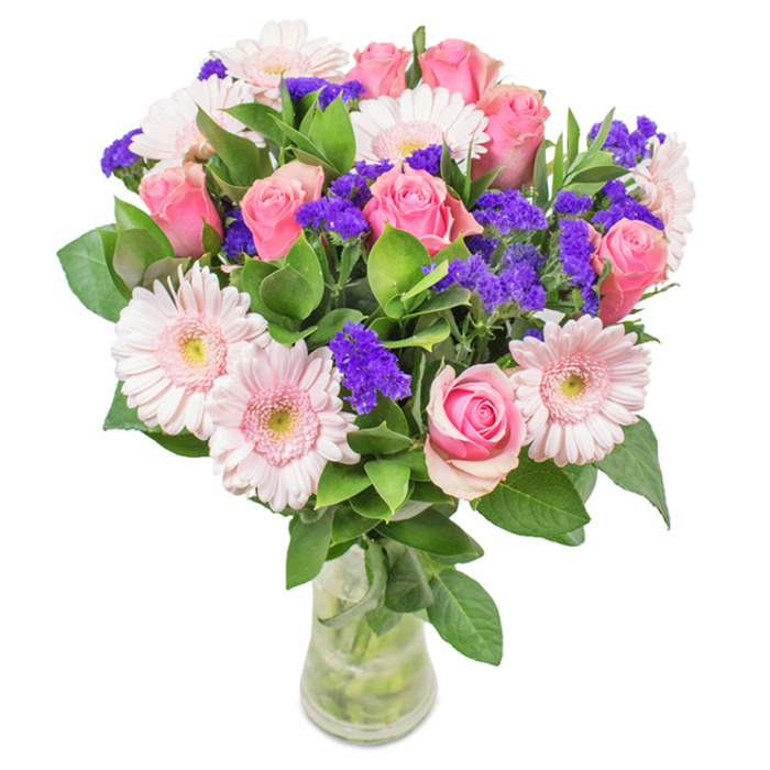 An exquisitely arranged floral bouquet from Palmers Green, showcased in a crystalline glass vase against a soft, neutral backdrop. Approximately seven to nine medium pink roses, many just beginning to unfurl in delicate spirals, form the heart of the arrangement, their petals tinted with graceful blush and classic elegance. Nestled among them, a handful of paler pink gerbera daisies with broad, rounded petals and almost silvery centres provide a luminous, airy touch. Interspersed throughout are clusters of vivid purple statice, their papery, textural blossoms bringing a vibrant pop of colour that enlivens the palette and deepens the visual interest. Below and between the blooms, lush deep green foliage creates a feeling of abundance, grounding the bouquet in the fresh vibrancy characteristic of Palmers Green's leafy streets. The transparent vase, with water glimmering among the stems, suggests a just-delivered freshness straight from a local artisan's hands. Ideal for birthdays, anniversaries, Mother's Day, or as a tasteful accent for a Palmers Green home or office, this bouquet conveys joyful celebration and tender affection-its harmonious design echoing the thoughtful, community-rooted service of neighbourhood florists.